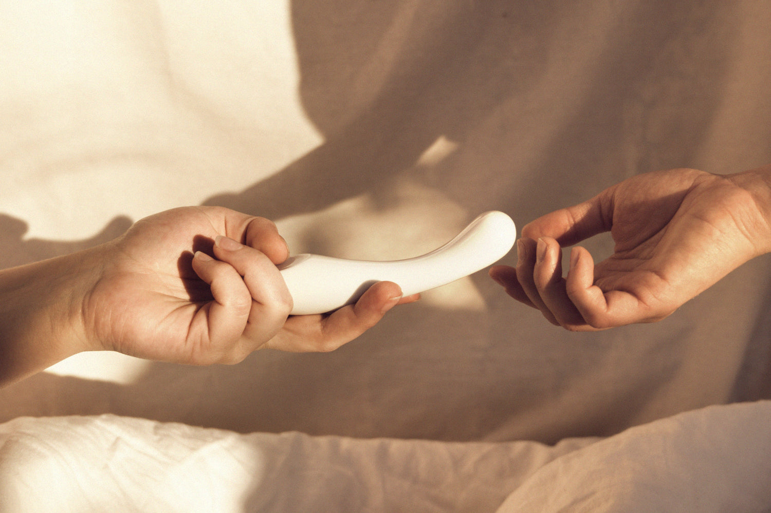 Studio Labim: Der Bildausschnitt zeigt die Hände zweier Personen. Die linke Hand hält den Dildo Clara in weiß. Die zweite Person greift ebenfalls nach dem Sextoy