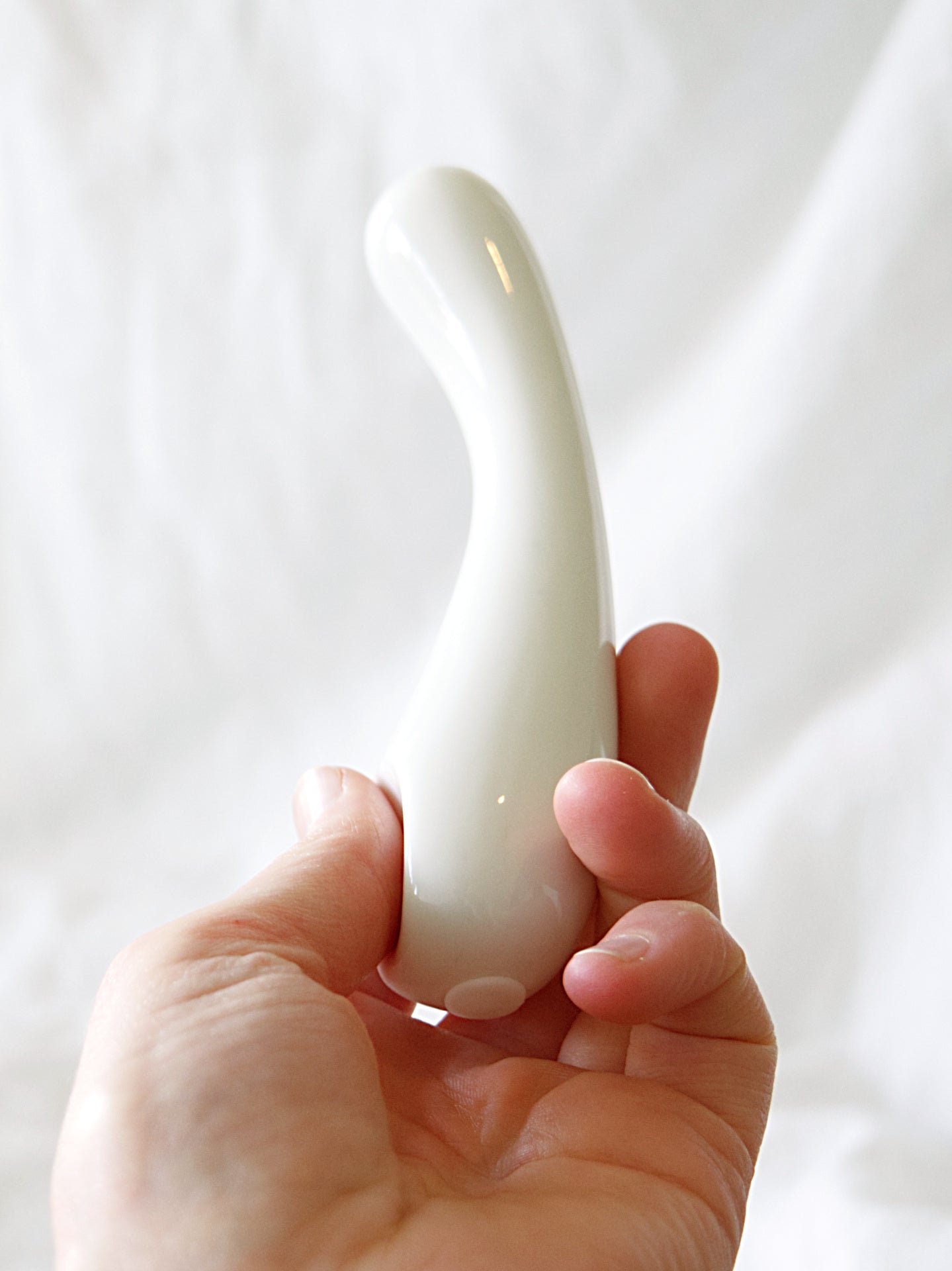 Die Nahaufnahme zeigt den Porzellan-Dildo "Clara" der Marke Labim in Weiß. Eine Hand hat das Sextoy vor die Kamera