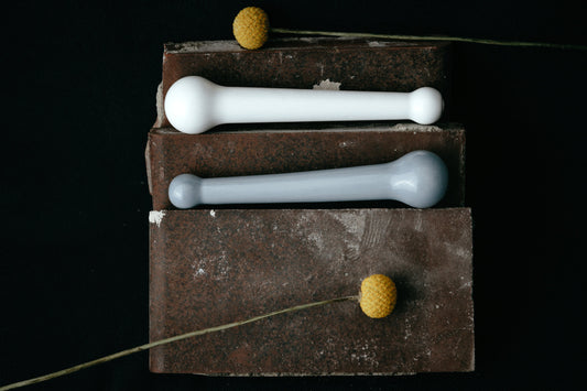 Studio Labim: Abgebildet sind die Dildos "Helen" aus Porzellan in den Farben weiß und blau. Die Sextoys ruhen für das Foto auf Ziegelsteinen auf zwei Ebenen und sind mit gelben Blumen dekoriert.