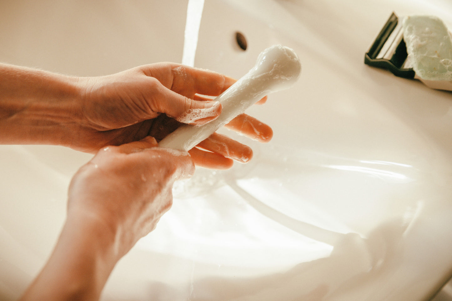 Studio Labim: Die Nahaufnahme zeigt eine Reinigung des Porzellan-Dildos "Helen" in weiß glasiert. Eine Person reinigt das Sextoy mit Wasser und einer milden Seife.