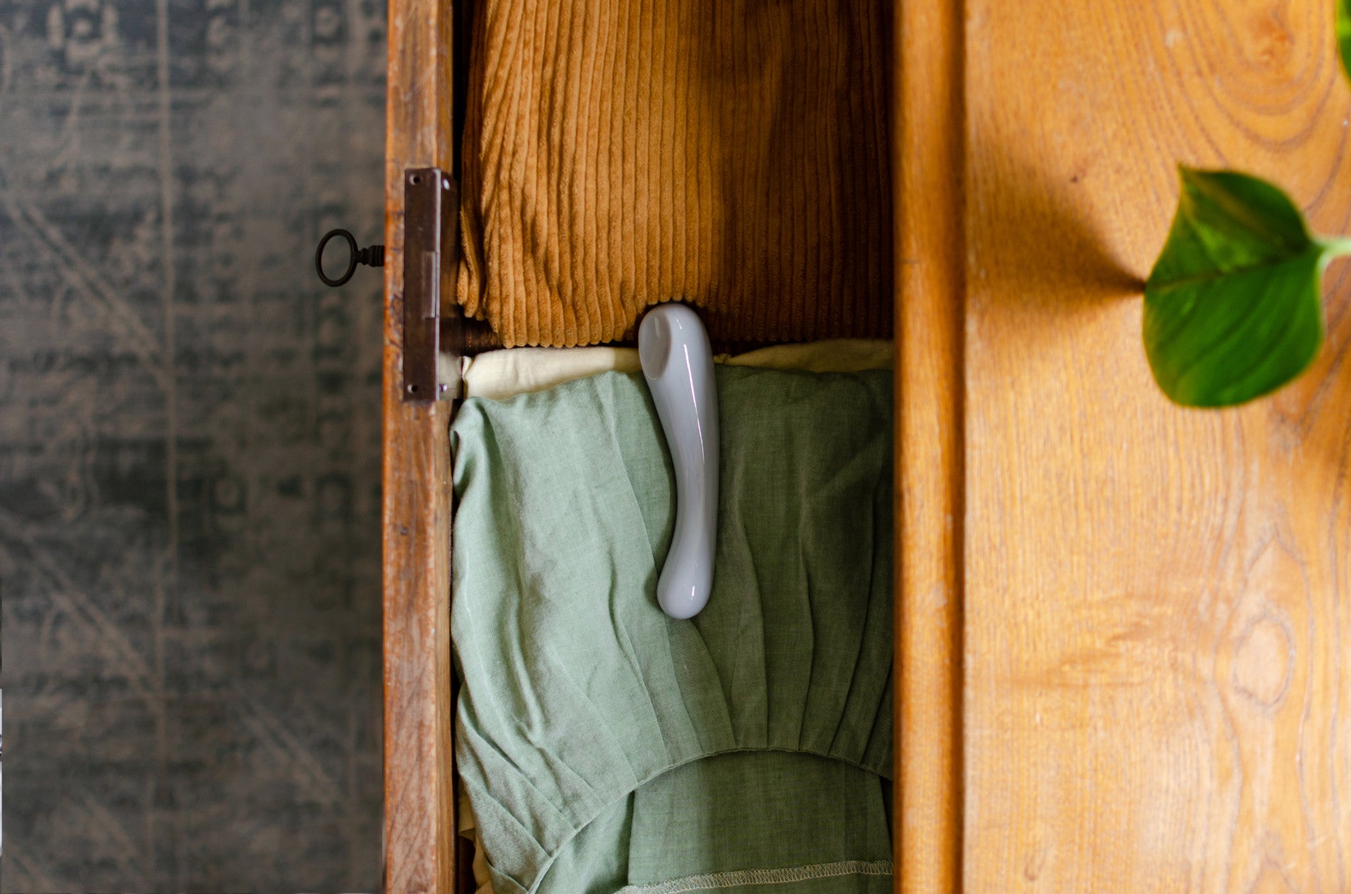 Der Bildausschnitt zeigt den Porzellan-Dildo "Clara" in Blau, der in einer Holzkommode verstaut ist 